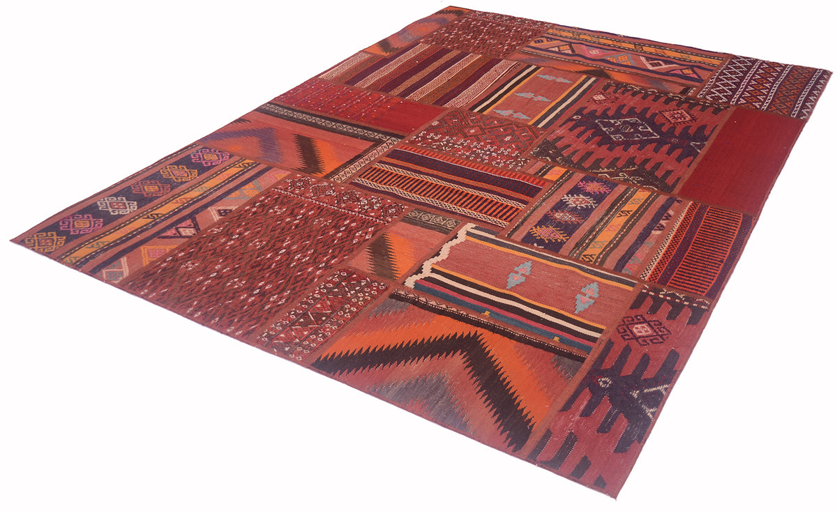 A rectangular patchwork-style rug with a Southwestern geometric pattern in shades of red, orange, brown, and black, shown from an elevated angle on a white background.