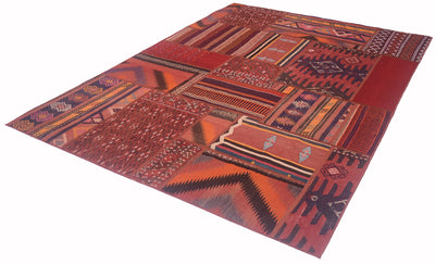 A rectangular patchwork-style rug with a Southwestern geometric pattern in shades of red, orange, brown, and black, shown from an elevated angle on a white background.