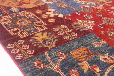 A close-up of a traditional patterned Afghan Patchwork design rug showing multiple colour-blocked sections in red, blue, and brown with floral and geometric motifs.
