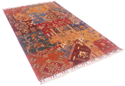 A rectangular hand-woven Afghan Patchwork area rug with a complex collage design in red, blue, orange, and beige, featuring traditional geometric and floral motifs and white fringe on the ends.