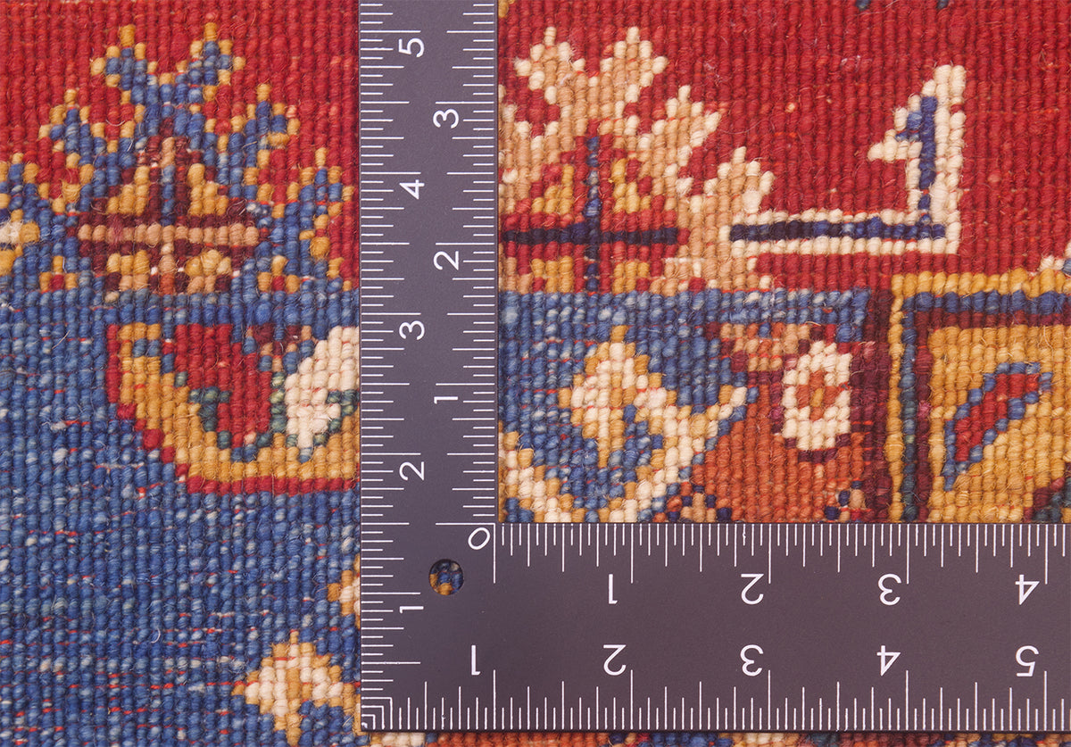 Close-up of the hand-knotted back of an Afghan Patchwork design rug with a dark ruler placed vertically and horizontally to show scale of the knotting, featuring a red, blue, and cream geometric woven design.