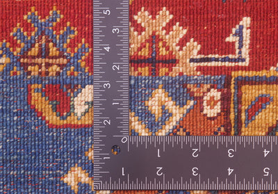Close-up of the hand-knotted back of an Afghan Patchwork design rug with a dark ruler placed vertically and horizontally to show scale of the knotting, featuring a red, blue, and cream geometric woven design.