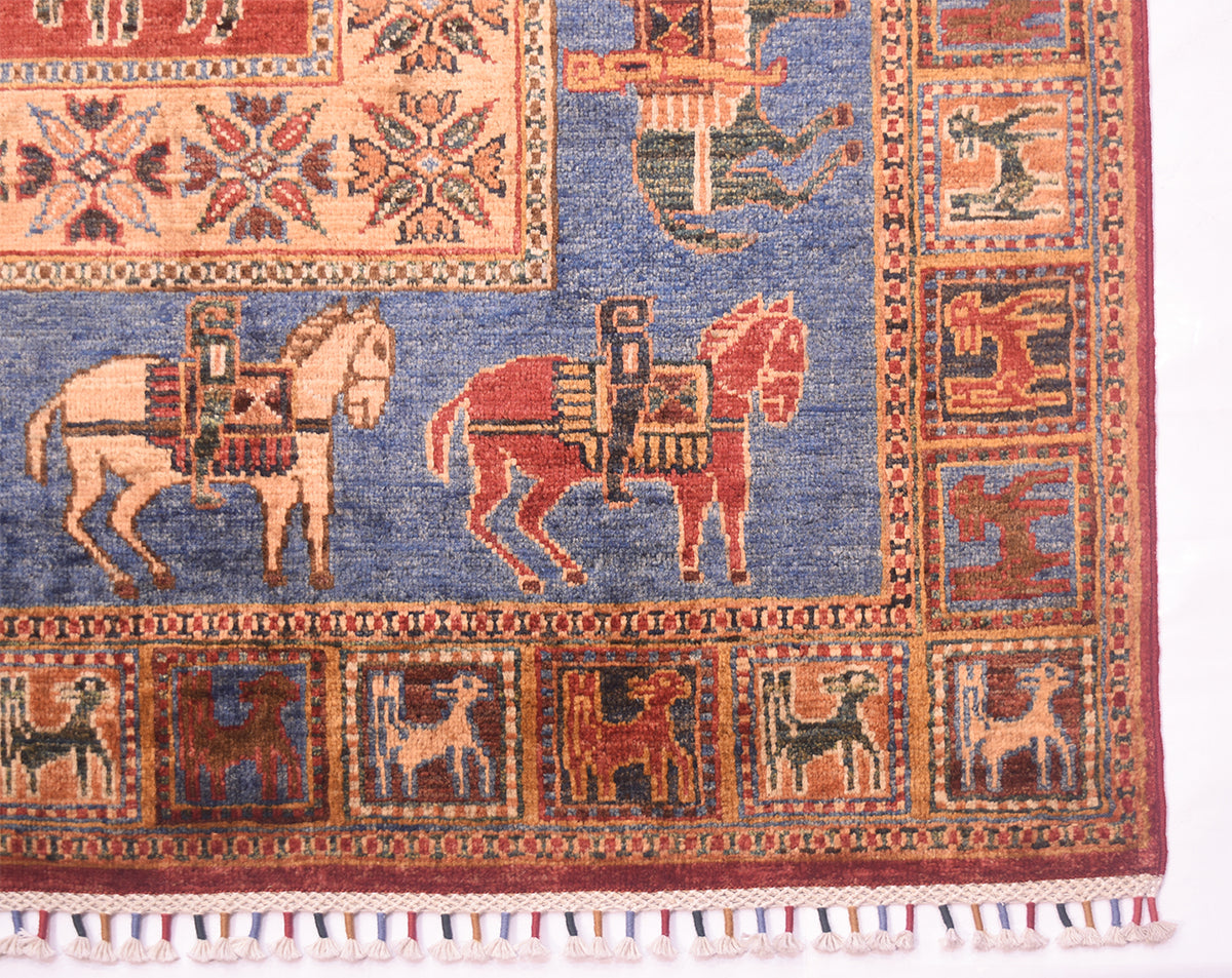 A close-up of a Handmade Afghan Pazyryk carpet showing a blue field with two horse figures, bordered by red and beige geometric and animal motifs, with fringe visible along the bottom edge.