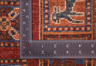 Close-up of a Handmade Afghan Pazyryk carpet with a dark metal L-shaped ruler showing measurements in centimetres and inches to indicate scale of the knotting.