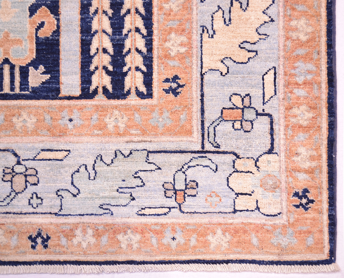 Close-up of a corner of an Afghan area rug showing its detailed woven pattern, featuring a peach border, a light blue field, and navy blue accents.