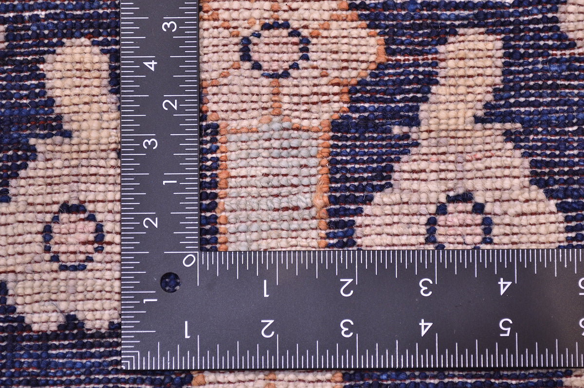 Close-up of the hand-knotted weave of a pictorial Afghan Bakhshaish Rug with a dark ruler placed over it to show scale of the knotting, featuring a woven design in beige, navy, and orange-brown.