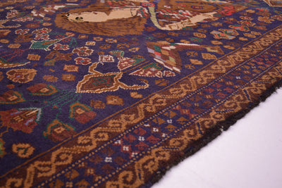A close-up of an intricate traditional afghan rug with a dark blue field, brown borders, and multi-colored motifs including a central figure.