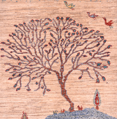 A close-up of a pictorial Loribaft small rug featuring a stylised tree with brown branches and small blue and red leaf-like details, set against a warm beige background with small bird and tree motifs.