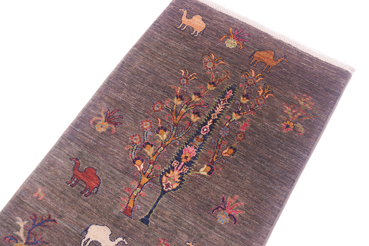 A close-up of a textured Pictorial grey Loribaft runner with a pewter base, featuring a central stylised tree with pink and orange floral details and various desert animal motifs including camels in tan, red, and cream.