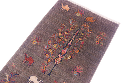 A close-up of a textured Pictorial grey Loribaft runner with a pewter base, featuring a central stylised tree with pink and orange floral details and various desert animal motifs including camels in tan, red, and cream.