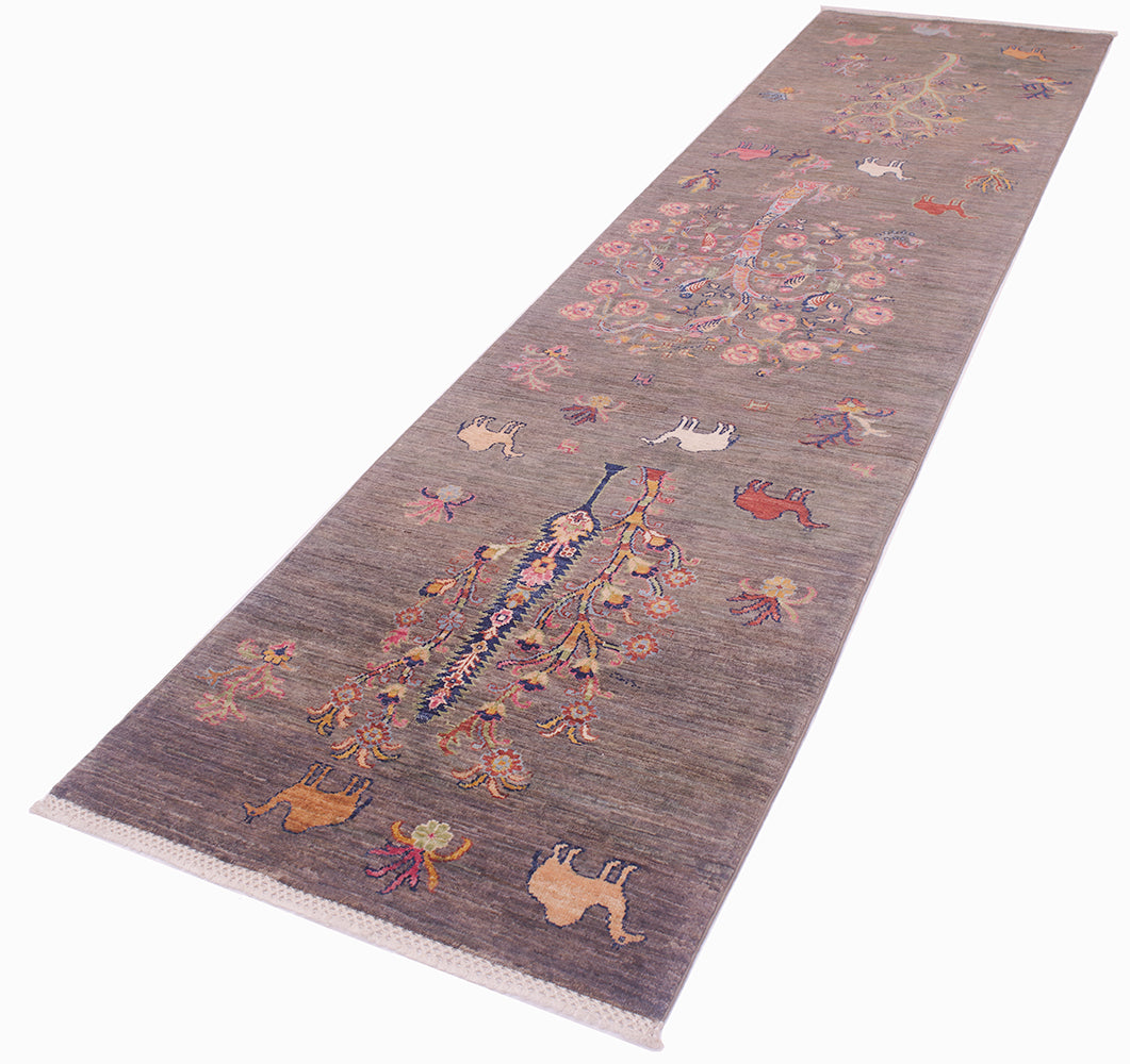 A long rectangular Pictorial grey Loribaft runner shown at an angle on a white background. The rug has a grey base with a detailed folk-art style design featuring a large central bird, smaller animals, and floral motifs in pink, orange, blue, and cream.