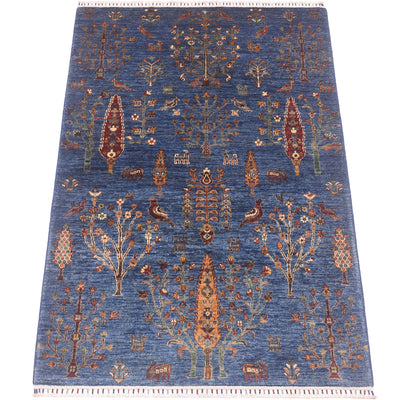 A 6x4 rectangular pictorial blue Loribaft rug with an intricate traditional tribal pattern featuring stylised trees, birds, and geometric motifs in rust, beige, and brown, finished with a fringed edge.