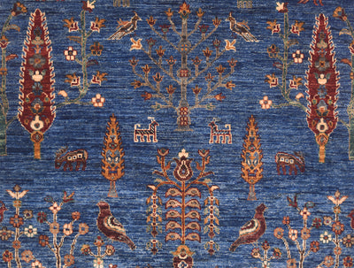A close-up of a patterned pictorial Afghan Loribaft rug featuring a blue field with ornate motifs including birds, trees, floral elements, and small animal figures in rust, beige, and cream tones.