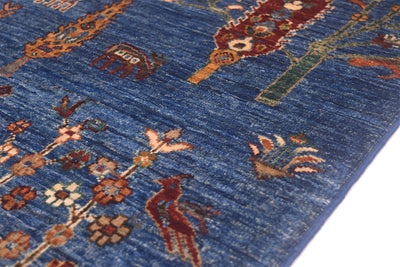 A close-up of a blue patterned Afghan pictorial rug with traditional motifs including birds, floral elements, and abstract shapes in rust, beige, green, and cream.
