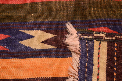 Close-up of a handwoven Afghan kilim runner rug showing its striped pattern in orange, navy blue, brown, and beige, with a fringed edge.