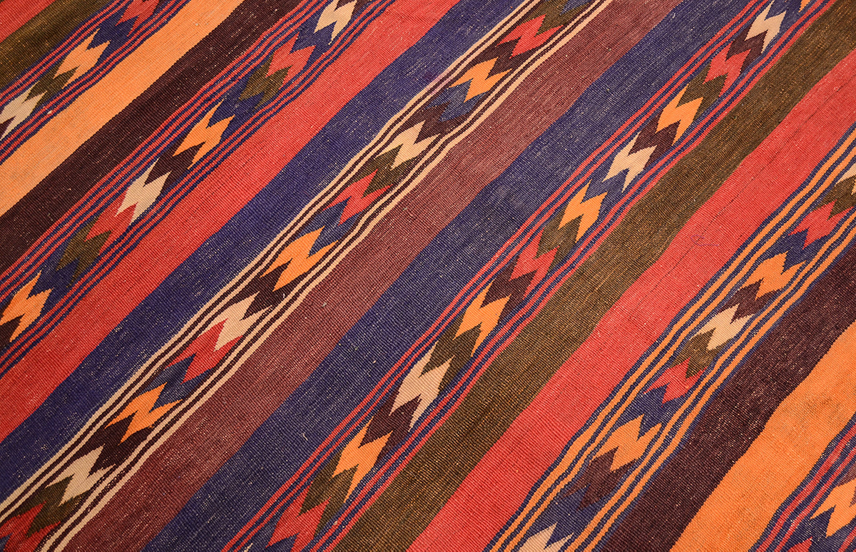 A close-up of a handwoven Qala-i-Nau Kilim wide runner rug with stripes in rust red, navy blue, olive brown, orange, cream, and dark brown, featuring repeating geometric zigzag motifs.