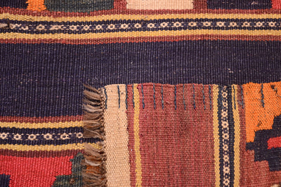 Close-up of a corner underside of a hand woven old Afghan kilim runner rug showing a dark navy blue field, patterned borders in cream, rust, and orange, and a fringed edge.