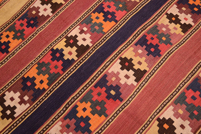 A close-up of a woven old Afghan kilim rug with diagonal stripes and geometric patterns in rust red, navy blue, orange, beige, and brown.