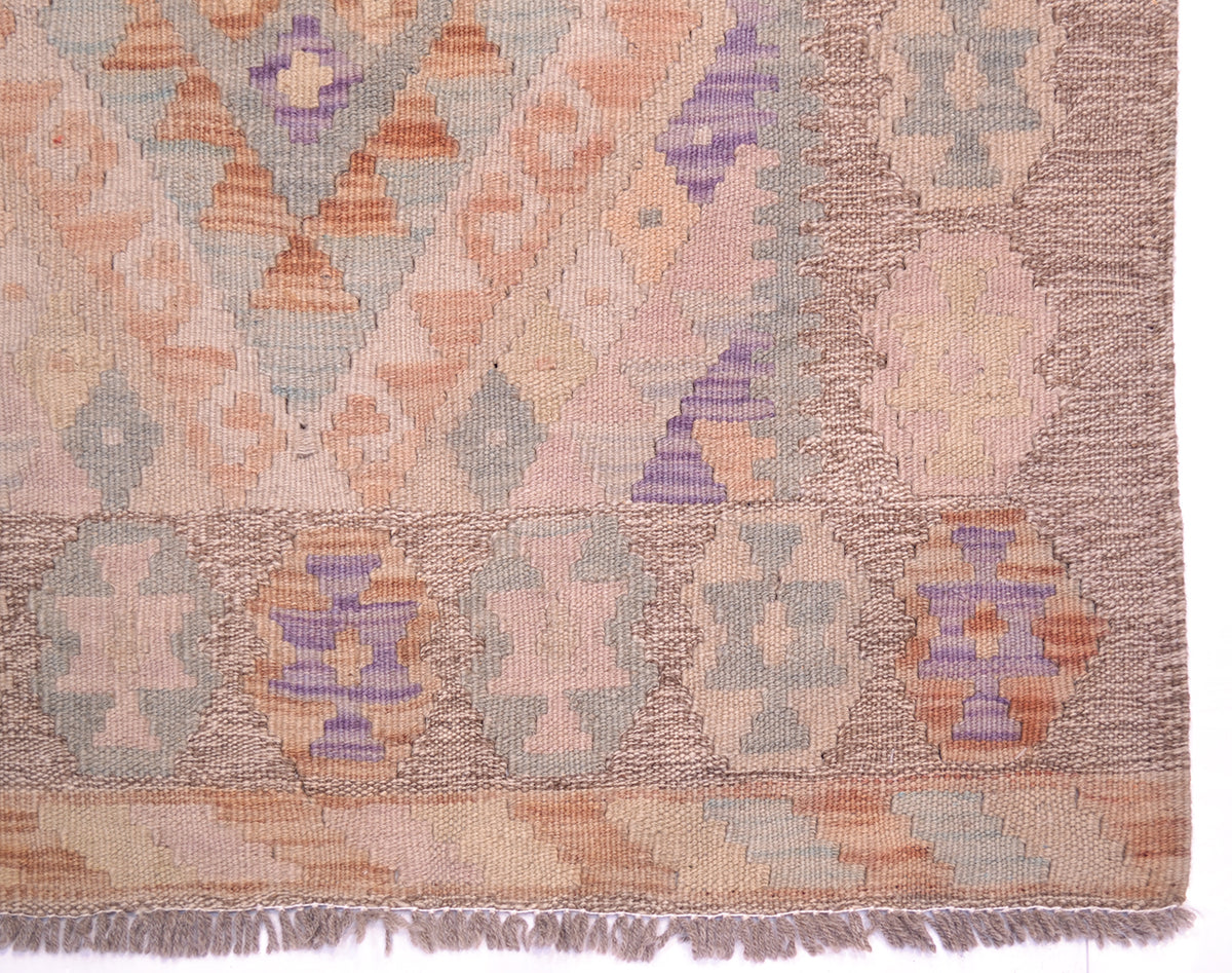 A close-up of a kilim runner showing its woven geometric pattern with shades of dusty pink, purple, orange, and gray on a beige background.