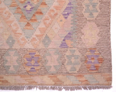 A close-up of a kilim runner showing its woven geometric pattern with shades of dusty pink, purple, orange, and gray on a beige background.