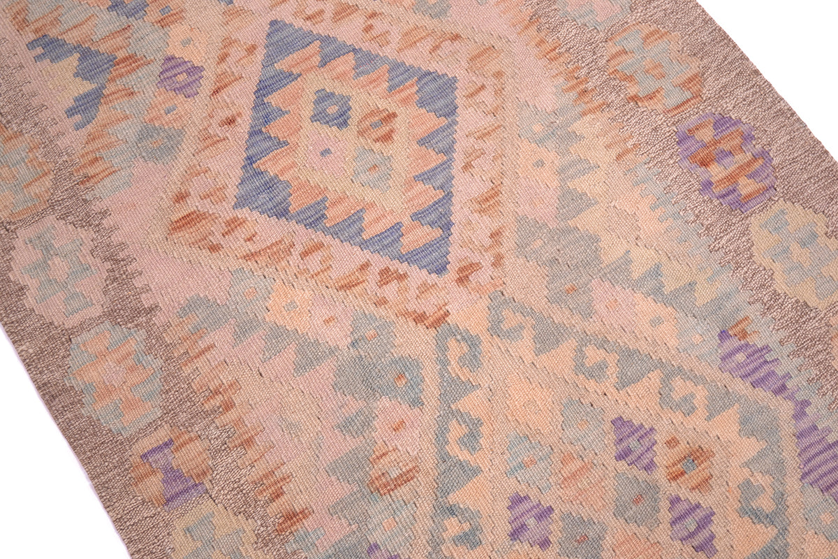 A close-up of a handwoven Soft colour Kilim runner with a dusty pink base and patterns in blue, purple, and orange, shown on a white background.