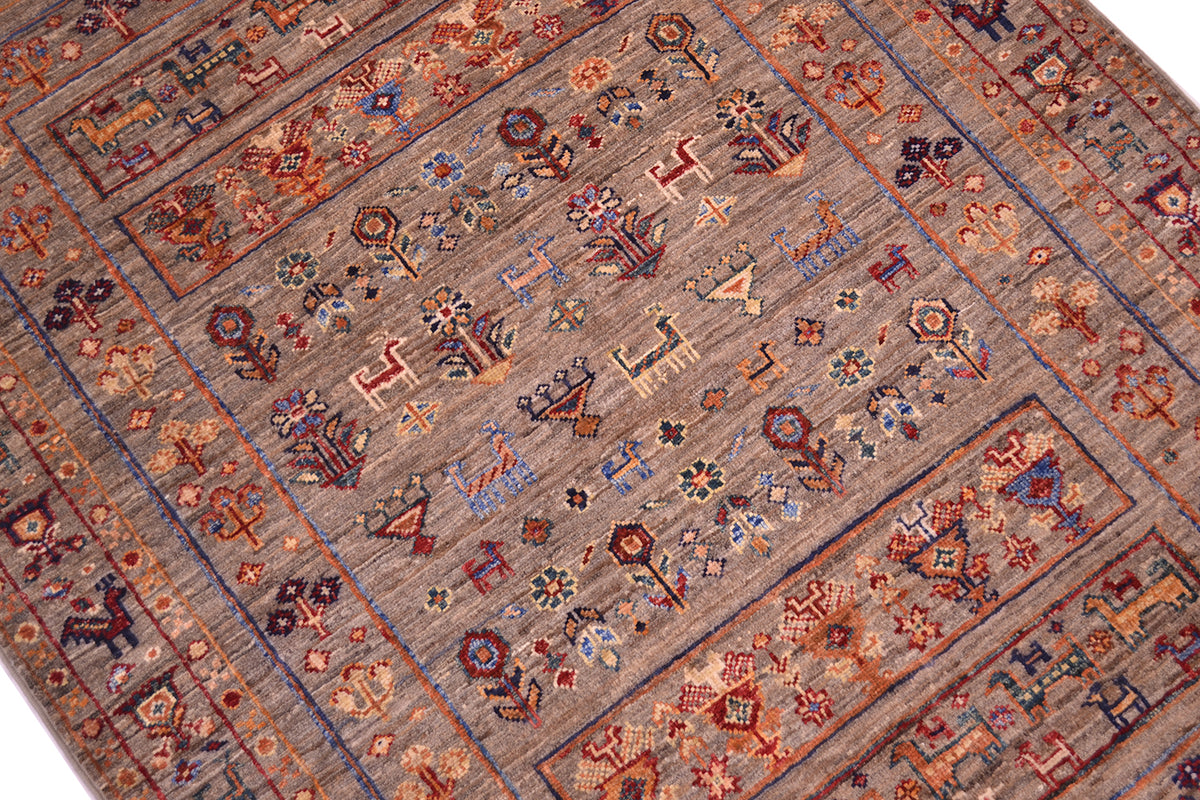 A close-up of a traditional handwoven modern Afghan Samarkand rug with a geometric and floral pattern in muted earth tones, including brown, beige, red, blue, and orange.