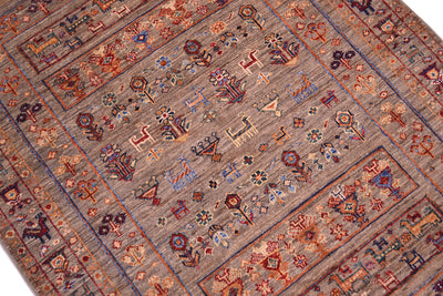 A close-up of a traditional handwoven modern Afghan Samarkand rug with a geometric and floral pattern in muted earth tones, including brown, beige, red, blue, and orange.