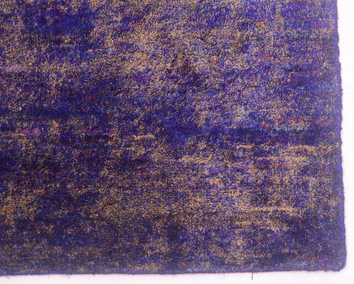 A close-up of a Sari Silk rug showing a mottled pattern of deep purple, blue, and tan/beige tones.
