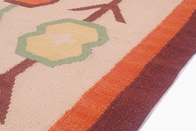 A close-up of a woven Scandi style rug showing its pattern and texture, featuring a cream base with geometric shapes in orange, brown, green, and yellow.