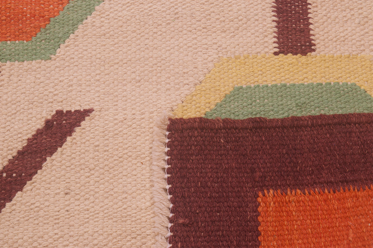 Close-up of the weave of a handwoven Afghan Scandinavian style Kilim rug showing a geometric pattern with a cream base, dark brown blocks, orange accents, and muted green and yellow details.