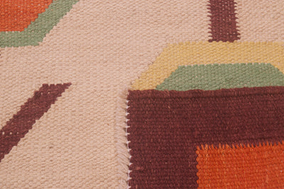 Close-up of the weave of a handwoven Afghan Scandinavian style Kilim rug showing a geometric pattern with a cream base, dark brown blocks, orange accents, and muted green and yellow details.