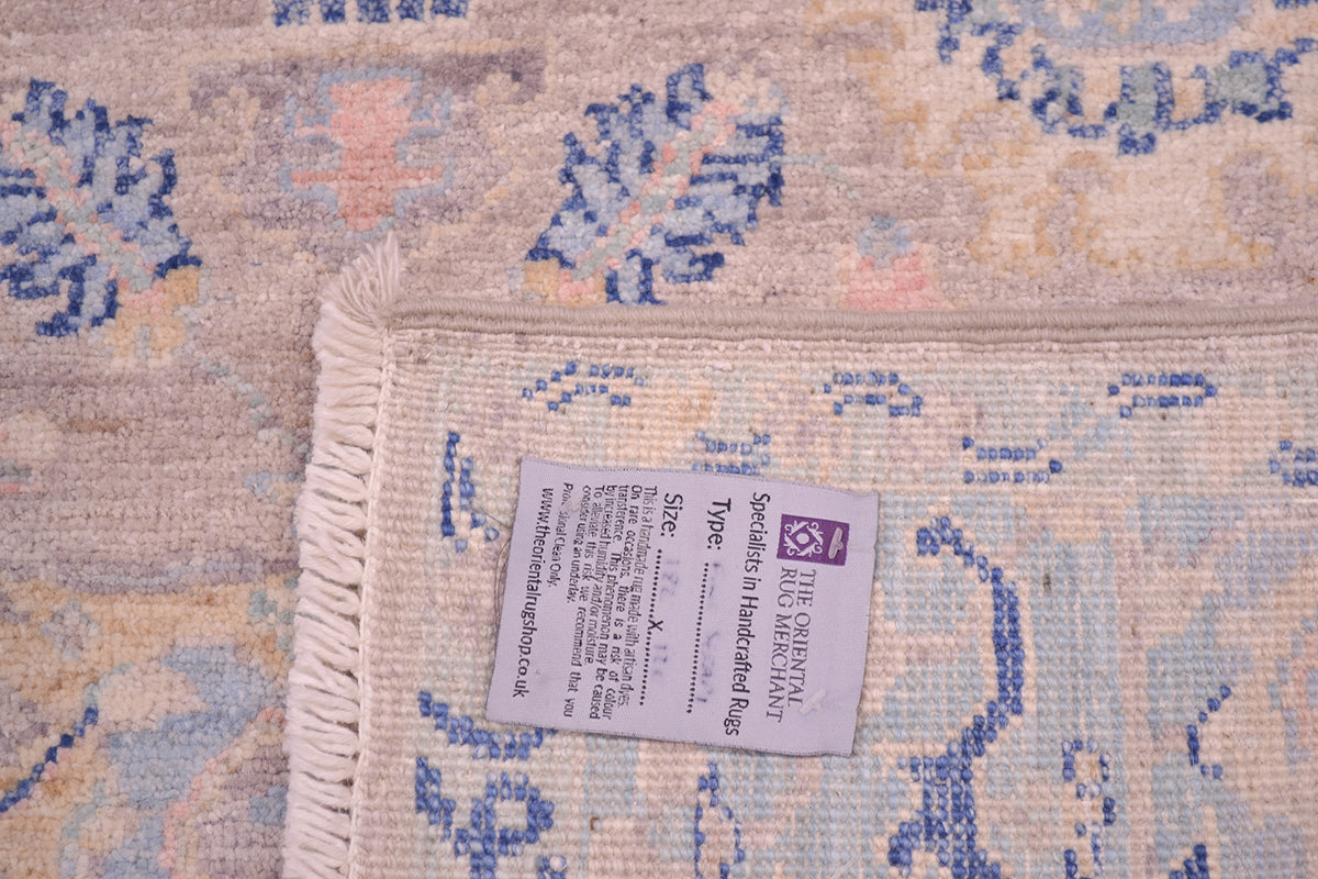Back of rug showing knotting and also detail of handwoven pile of main field with nuanced hues of yellow, pink and light and dark blue on a soft grey coloured main field. 