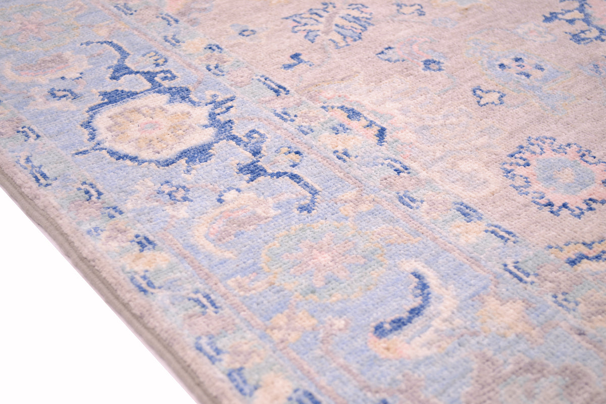 Detail of border of handknotted rug with light blue and duck egg coloured border background with cloudband pattern border and stylized leaves. Soft pastel tones throughout the colouration of this rug.