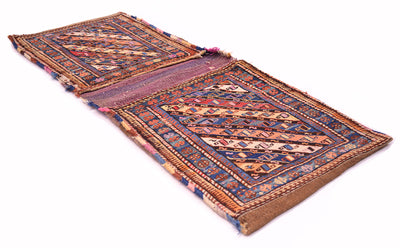 Antique khorjin rug laid flat with geometric blue, rust, and cream motifs; fringed ends