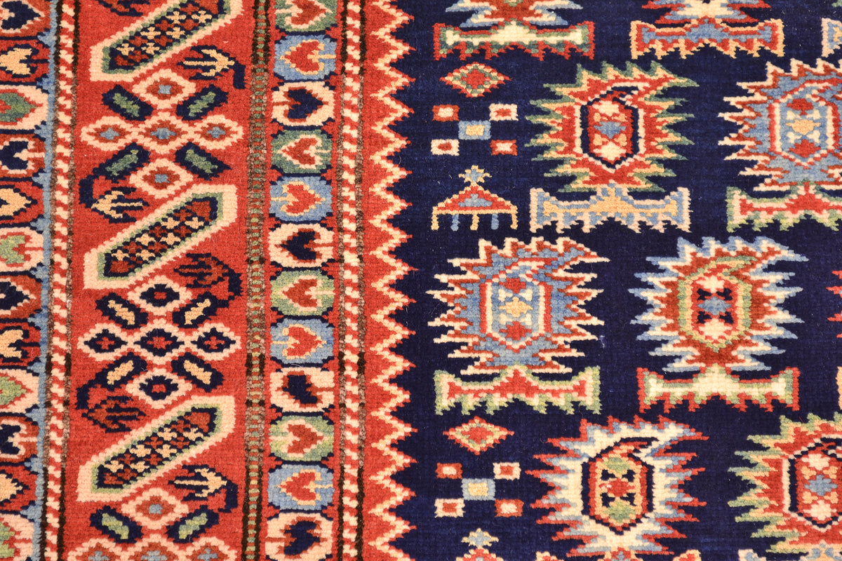 Close-up of a hand-knotted Afghan Shirvan rug with a dark navy blue field and bold geometric paisley motifs in rust red, cream, and light blue, bordered by red and blue patterned bands.