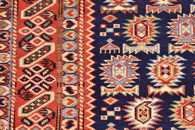 Close-up of a hand-knotted Afghan Shirvan rug with a dark navy blue field and bold geometric paisley motifs in rust red, cream, and light blue, bordered by red and blue patterned bands.