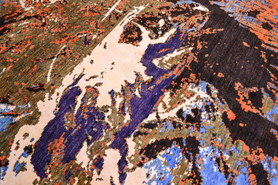 A close-up of a textured area rug featuring an abstract, organic pattern with large sections of deep purple, black, light beige, blue, and rust orange.
