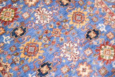 Detail view of main field of Sultanabad Design rug with blue field amd multiple floral detailing and floral blossoms in red, cream, light orange, gold and green. 