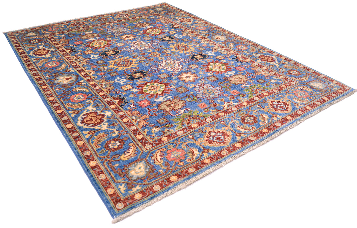 Angled view of Sultanabad rug on a white background showing glorious colours of red and blue with multiple secondary colours. All over floral field with famaous Persian design; handwoven in Afghanistan. 