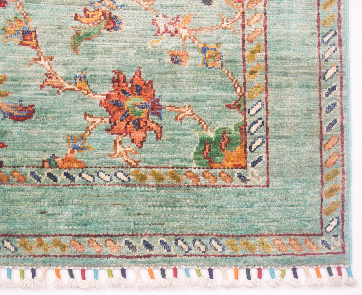 Corner detail of aghan rug with soft topaz colours and colourful geometric minor borders and floral filled field. Coloured yarn of warp thread make up bound fringe. 