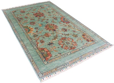Angled view of handknotted rug with topaz- light turquise main ground colour with linked flowerheads and and multiple leaves and blossom. Cotton warp threads are bound with coloured yarn. 