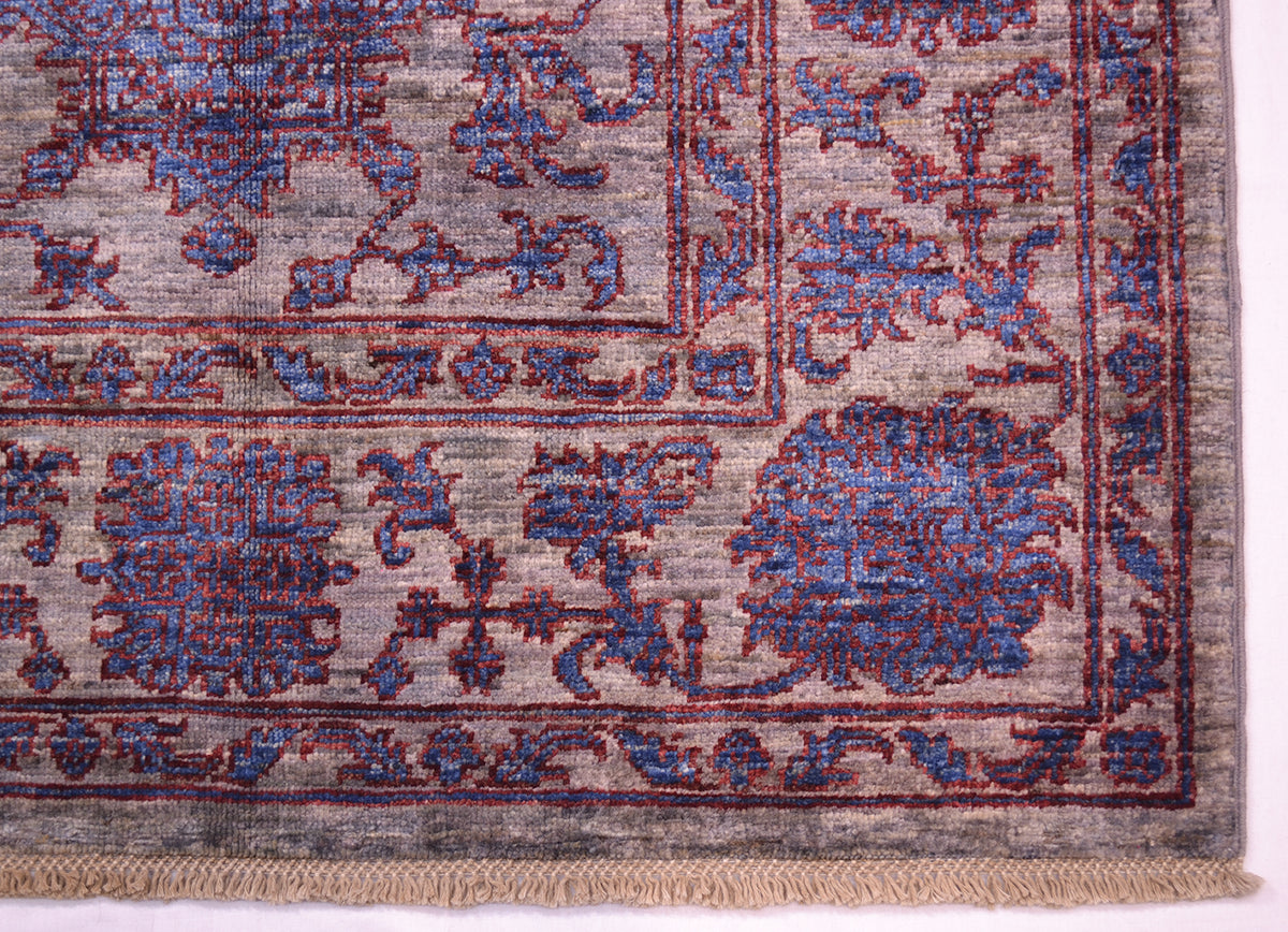 Corner detail of handmade rug with blues, grey and rich chestnut red detailing. Handknotted latticed cotton warps fringes.