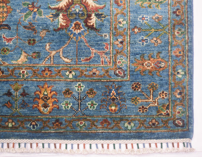 Corner detail of blue handmade rug with floral curvilinear designs with latticed fringes bound colourfully as a finishing features.
