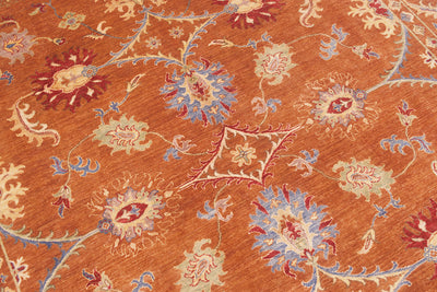 Detailed view of handknotted carpet with warming cinnamon/ amber toned main field with spacious floral motifs in red, blue, soft light green and cream. 