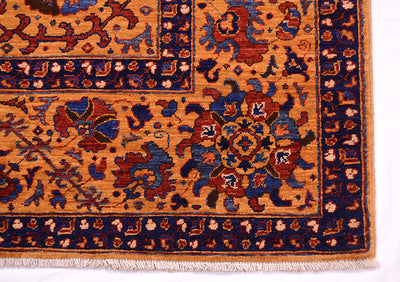 Close-up of a corner of a very fine handmade Suzani rug showing a warm amber field with navy blue borders and red, beige, and blue floral motifs, finished with cream fringe.