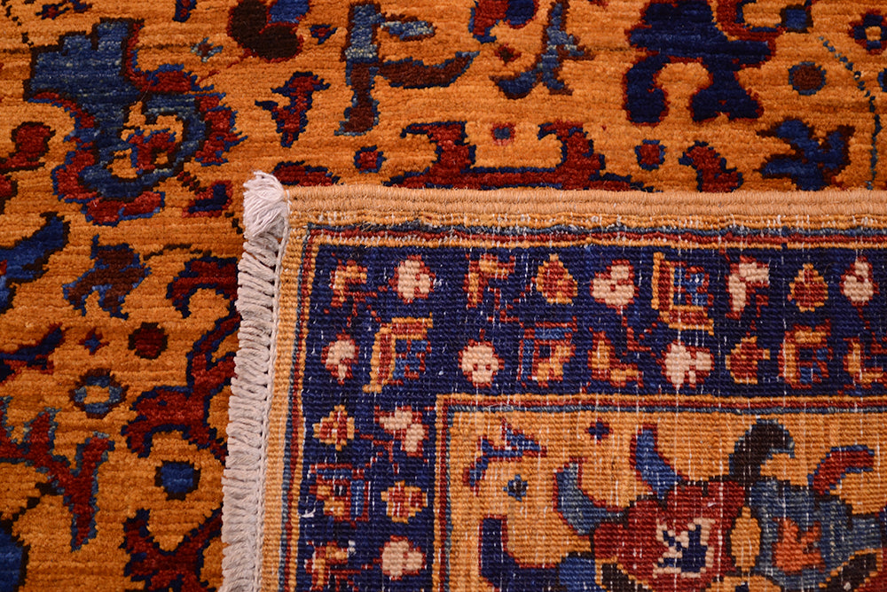 Close-up of the hand-knotted back of a very fine Afghan Suzani rug showing a warm orange field with dark blue, burgundy, and cream motifs, plus a white fringed edge.
