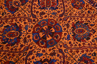 A close-up of a very fine handmade Suzani rug with a warm amber ground and detailed floral medallions in blue, burgundy red, and dark brown.