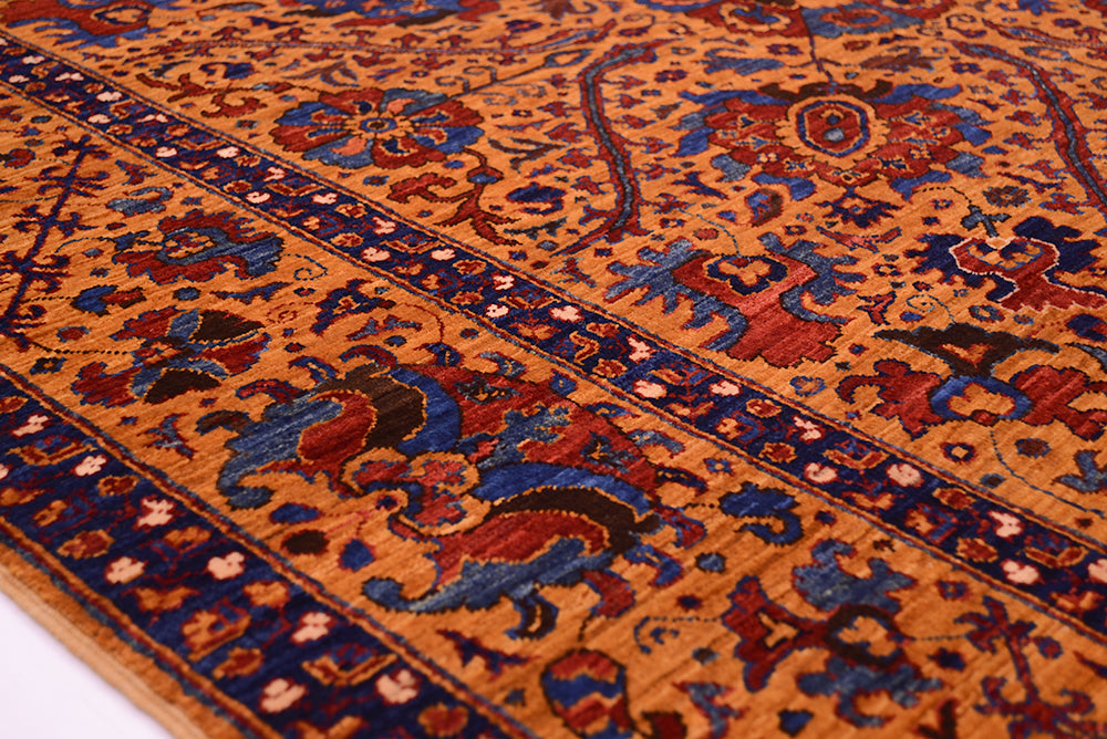 A close-up of an ornate very fine handmade Suzani rug with a warm amber field, deep blue borders, and red and beige floral motifs.