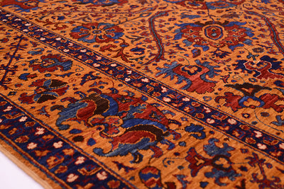 A close-up of an ornate very fine handmade Suzani rug with a warm amber field, deep blue borders, and red and beige floral motifs.