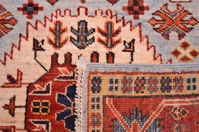 Close-up of a hand-knotted antique style Taimani runner showing detailed patterns, including a house motif in rust red, blue, and beige, alongside a light blue field and cream fringe.